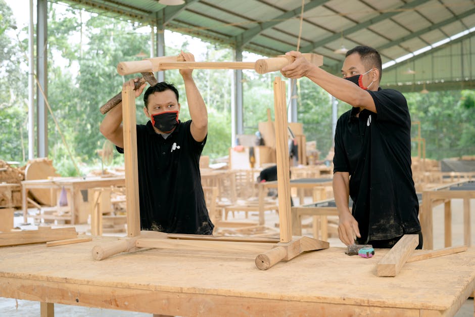 Two carpenters working on assembling a wooden frame in a spacious workshop.