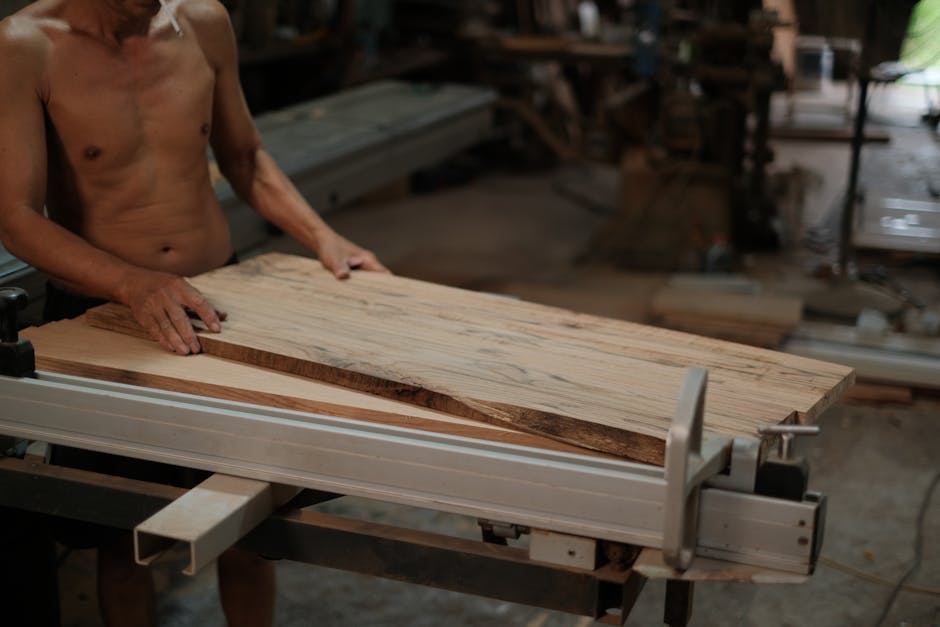 A shirtless adult using woodworking machinery in a workshop, focusing on craftsmanship and manual labor.