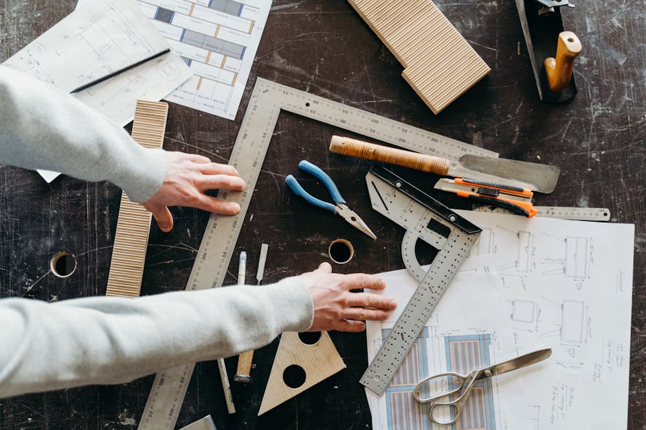 Hands arranging carpentry tools and blueprints on a workshop table, highlighting woodworking and design process.