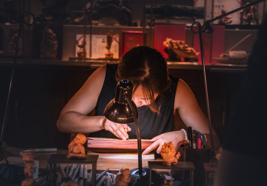 Focused artisan intricately engraving wood by lamp light, showcasing traditional craftsmanship in a cozy workshop.