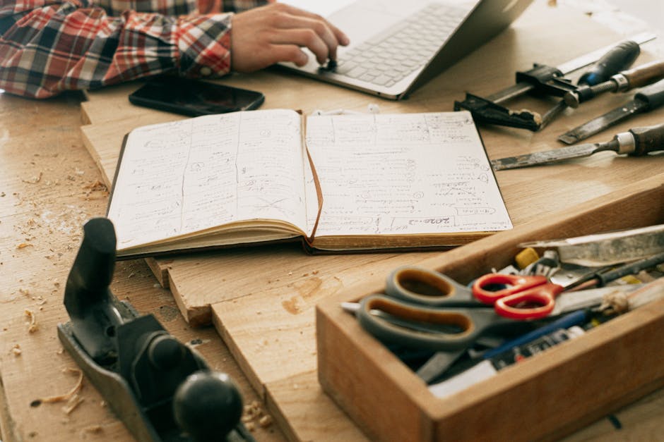 A woodworker's desk with tools, notebook, and laptop, showcasing creativity and craftsmanship.